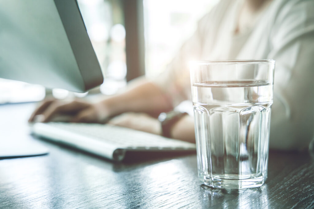 someone with a glass of water next to their keyboard